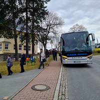 Ein Reisebus hält am Straßenrand vor der Grundschule Hormersdorf und Menschen steigen aus.